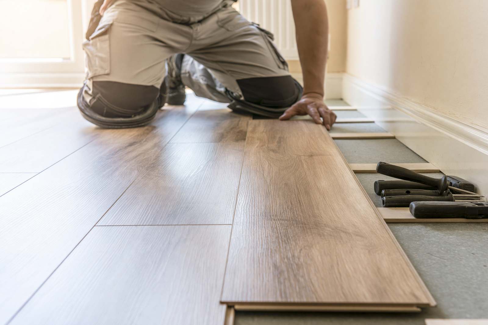 A fitter laying wood-effect flooring planks, with tapping block and pull bar on the underlay