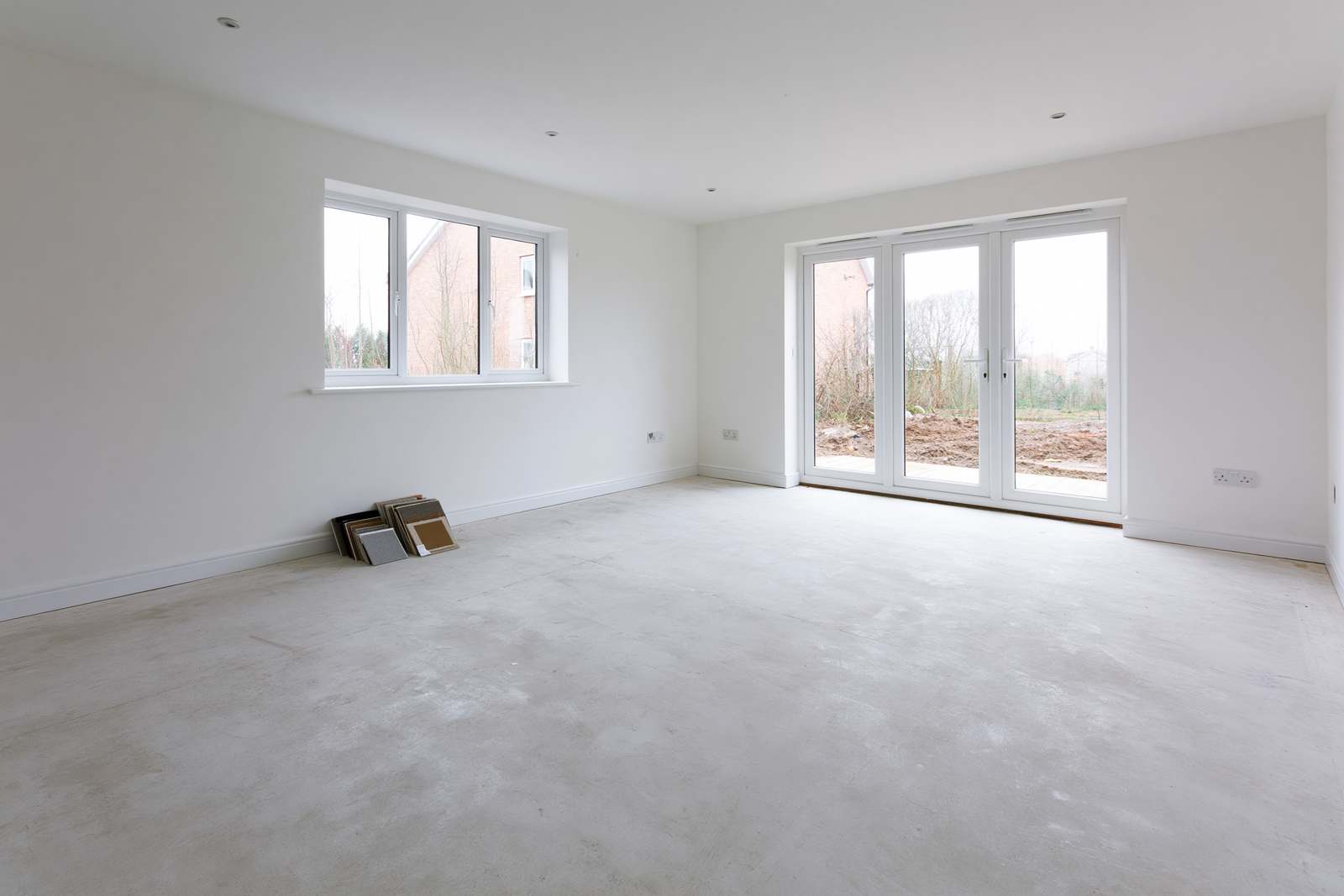 An empty new-build living room with a bare concrete subfloor and French doors, awaiting flooring